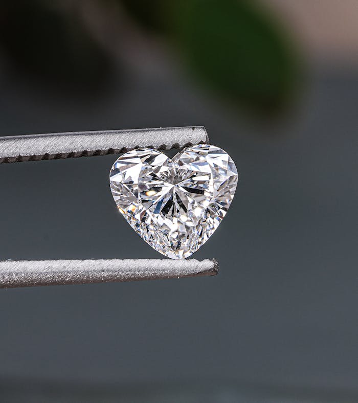 Detailed close-up of a heart-shaped diamond held in tweezers, showcasing its brilliance.