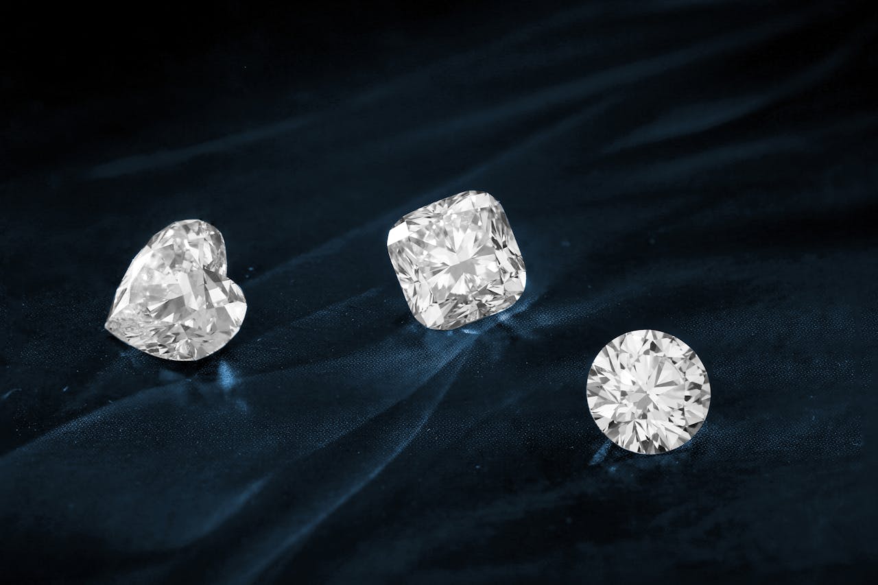 Three exquisite diamonds featuring heart, cushion, and round cuts displayed on dark fabric.